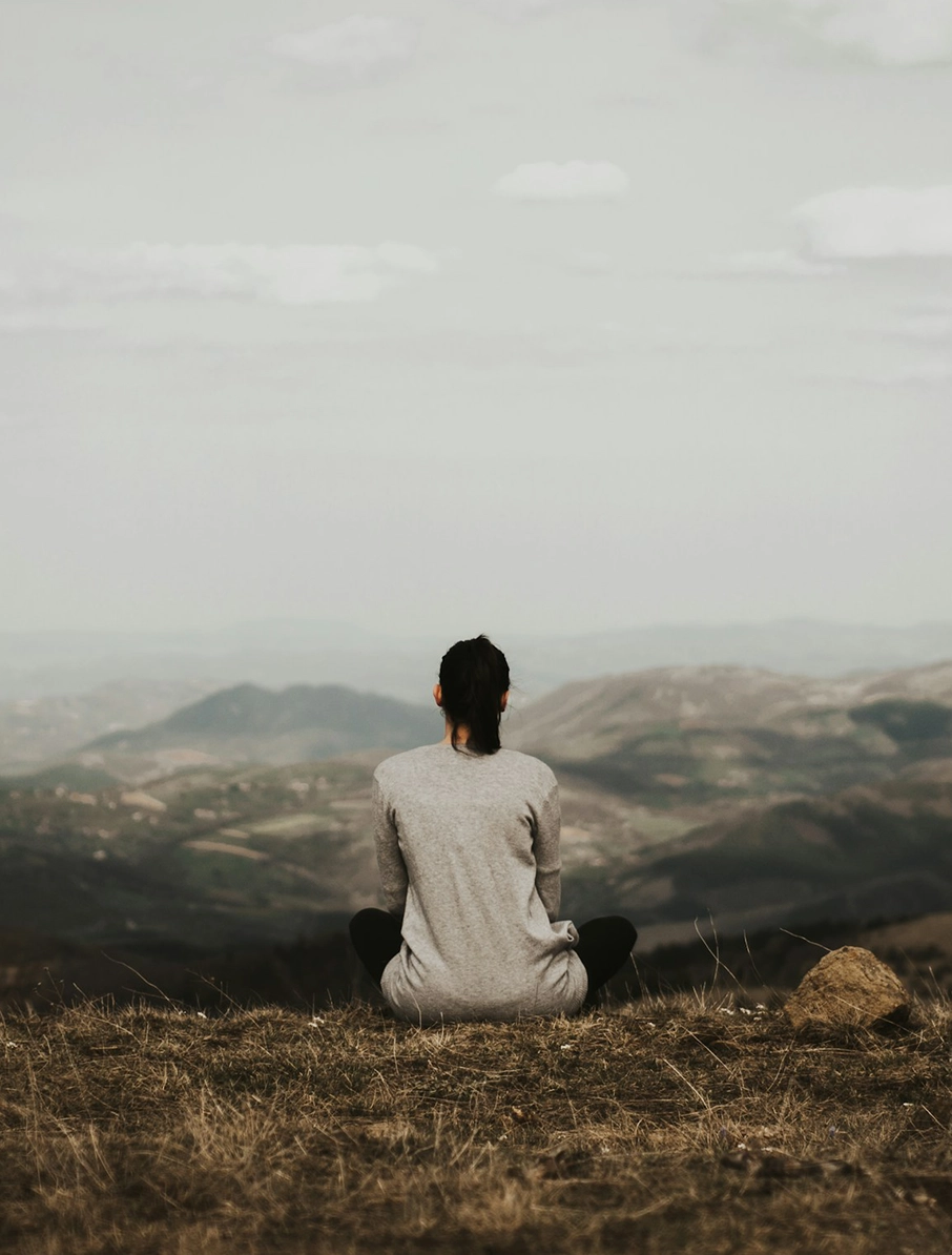 A young woman with her back to camera, sitting on a mountaintop